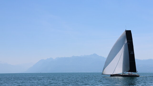 View of a sailboat sailing on Lake Geneva with the Alps in the background near Morges, Vaud, Switzerland.