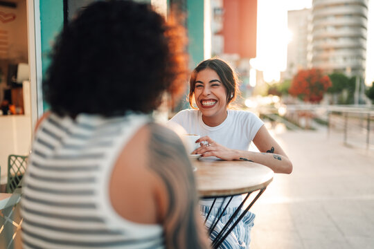 Friends enjoying conversation and laughing together at an outdoor cafe on a sunny afternoon in the city