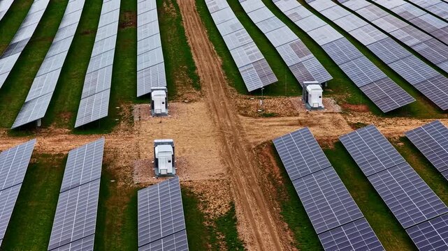 Aerial view of rows of solar panels in a large renewable energy farm with power inverters and dirt access paths in Latvia.