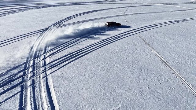 Aerial view of a red car performing a drift maneuver on a vast snow-covered field in Latvia.