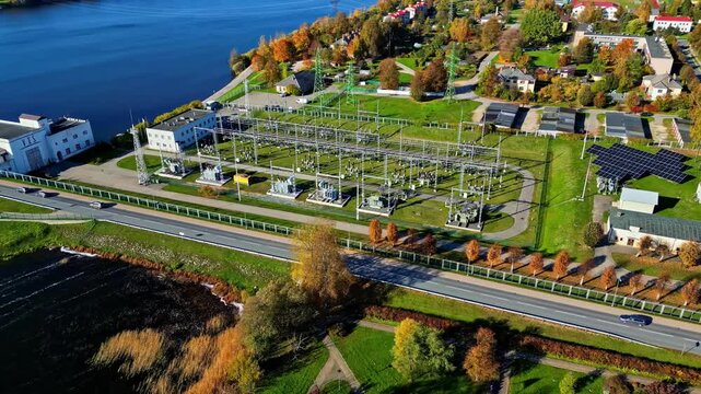 Aerial view of an electrical substation with transformers and power lines situated near a river and road in Riga, Latvia.