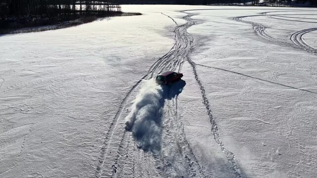 Aerial view of a car driving across a frozen snow-covered lake leaving deep tire tracks in the fresh snow in Latvia.