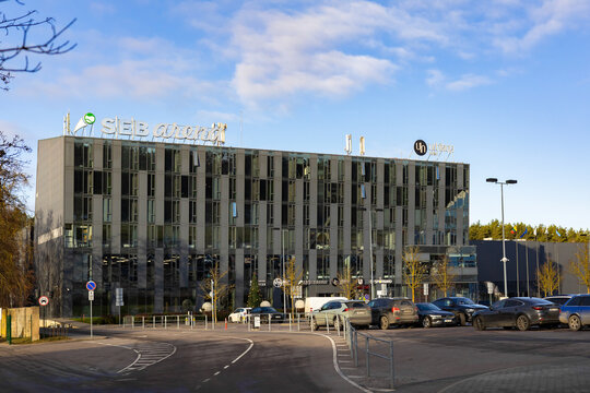 Vilnius, Lithuania - December 23 2025: Modern SEB Arena business complex and hotel, glass facade reflecting soft afternoon sunlight under partly cloudy blue sky, parked cars and quiet street scene.