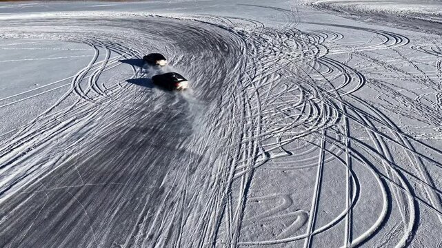 Aerial view of two cars drifting on a snow-covered track with tire tracks visible on the frozen surface in Latvia.