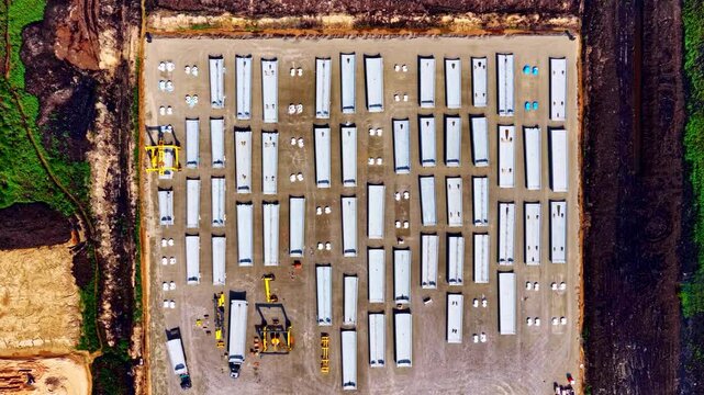 Aerial view of a large industrial storage yard filled with rows of white shipping containers and trailers arranged on a paved lot in Riga, Latvia.