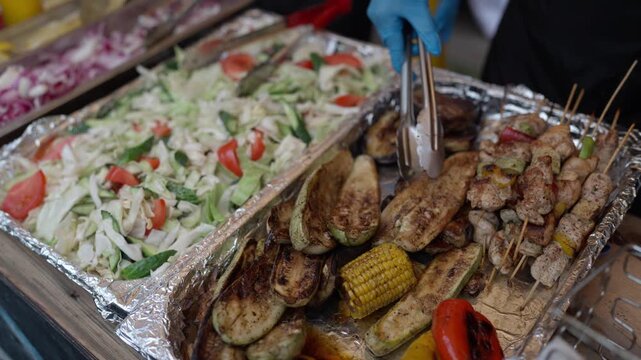 The seller sells grilled meat and vegetables. hands close up. Street food festival. Grilled meat and vegetables and fresh vegetables are on the counter at a street food establishment.