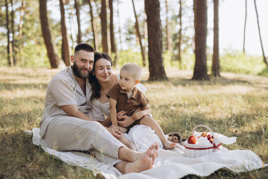 Happy family enjoying summer picnic in a sunny forest, parents and child bonding on blanket outdoors