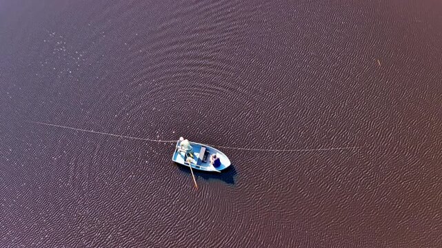 Aerial view of a small fishing boat with a person rowing on dark rippling water in Riga, Latvia.