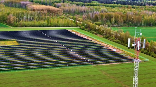 Aerial view of a solar farm with rows of photovoltaic panels and a telecommunications tower situated in the rural landscape near Riga, Latvia.