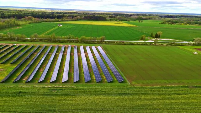 Aerial view of rows of solar panels installed in a green field surrounded by agricultural land and trees in Riga, Latvia.