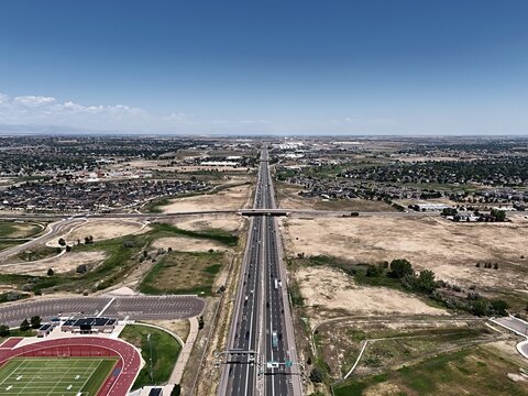 Aerial view of a multi-lane highway stretching through suburban neighborhoods and open fields under a clear blue sky in Thornton, Colorado, United States.