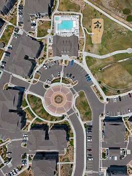 Aerial view of a modern residential apartment complex featuring a circular roundabout, parking lots, a swimming pool, and a playground in Thornton, Colorado, United States.