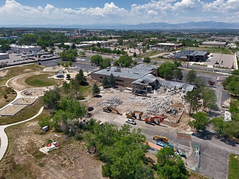 Aerial view of a demolition site with heavy machinery and excavators clearing rubble from a partially destroyed building near a park in Thornton, Colorado, United States.