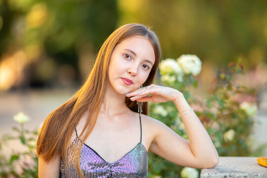 Elegant young woman posing among blooming pink roses in a summer garden. Romantic beauty portrait with long hair, stylish outfit and natural floral background, lifestyle concept.