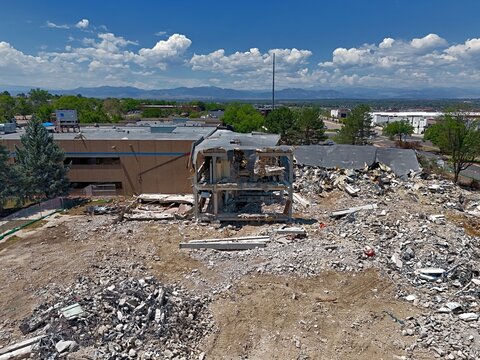 Aerial view of a demolition site with piles of rubble and a partially destroyed building structure under a blue sky in Thornton, Colorado, United States.
