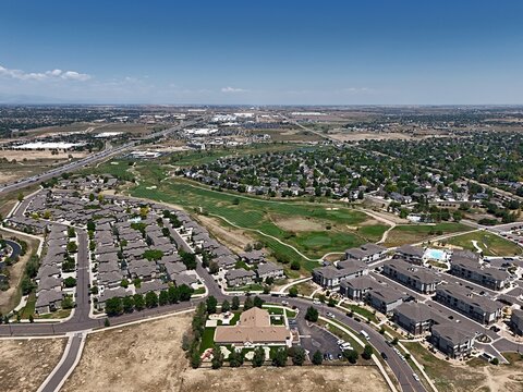 Aerial view of a suburban residential neighborhood with houses, apartment complexes, a golf course, and a highway in the distance in Thornton, Colorado, United States.
