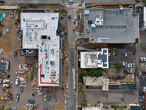 Aerial view of a construction site with building materials and machinery alongside an existing urban area with parking lots and buildings in Boulder, Colorado, United States.