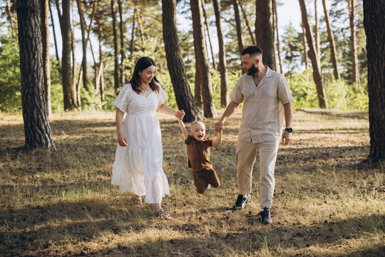Family enjoying quality time outdoors, parents holding toddler sons hands, swinging him in the air on a nature walk