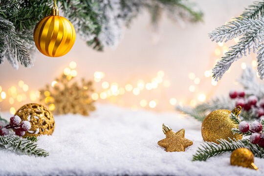 Glittering gold ornaments and snowflakes rest on snowy ground with frosted pine branches and soft glowing lights. Winter Christmas Holiday Decoration Background