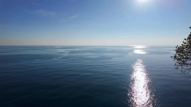 Calm mediterranean sea with soft sunlight reflection shimmering across water toward distant horizon.