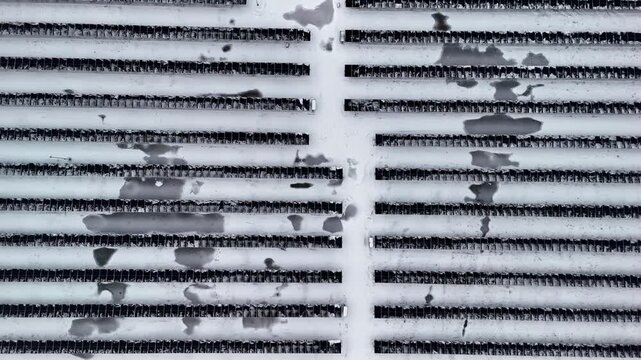 Aerial view of rows of solar panels partially covered in snow with patches of melting ice in a field in Latvia.