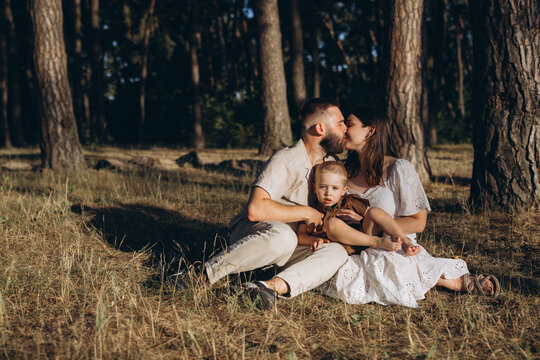 Family with young child sitting in forest enjoying summer sunset and showing love and togetherness