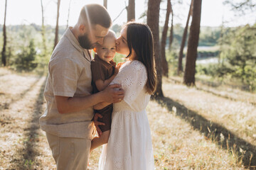 Fototapeta premium Young family expressing love and togetherness with son during summer outing in a sunlit forest