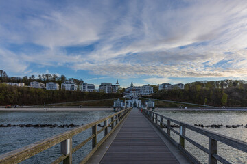 Fototapeta premium Direct perspective looking down an empty wooden pier towards multi-story hotels and a dome complex at twilight