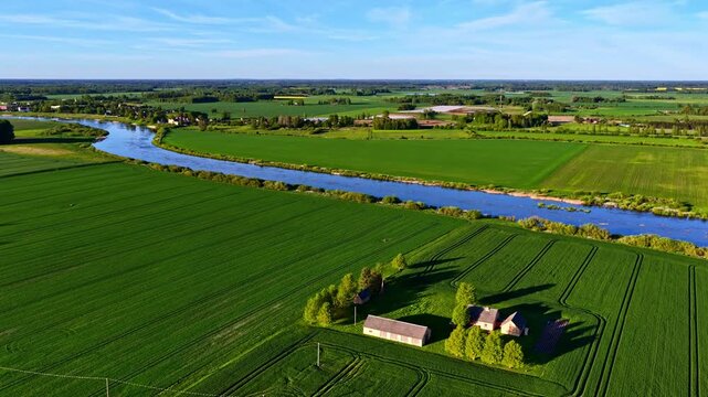 Aerial view of a river winding through green fields and a small farmstead in the countryside of Riga, Latvia.