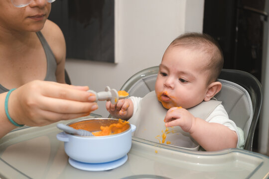 Beb&eacute; ni&ntilde;o comiendo papilla de zanahoria en la silla