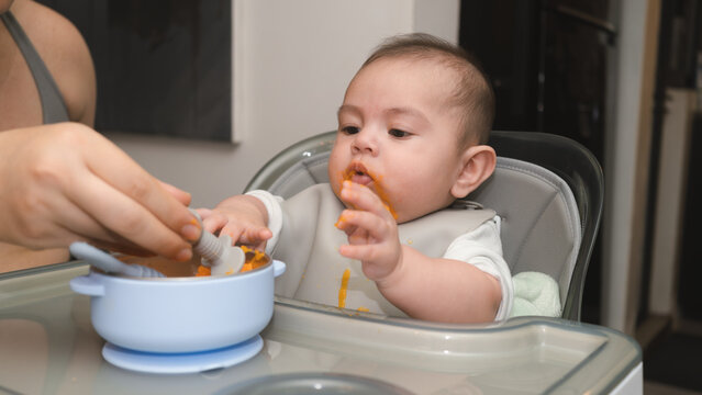Beb&eacute; ni&ntilde;o comiendo papilla de zanahoria en la silla