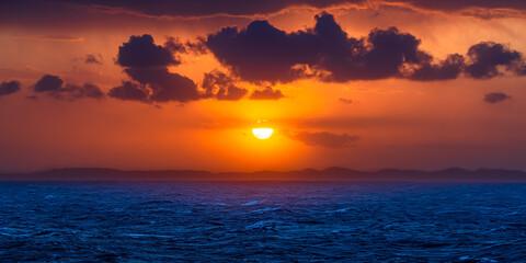 Dramatic ocean sunset with vibrant orange sky and dark clouds over the horizon © Dan Johnson Photos