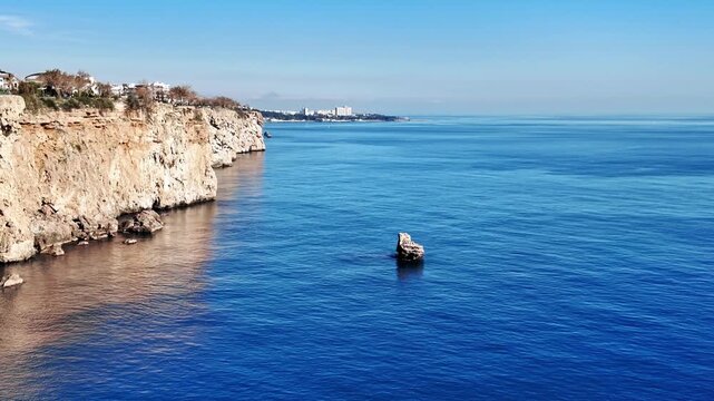 Camera pans across rugged limestone sea cliffs and calm blue mediterranean water in antalya coastline.