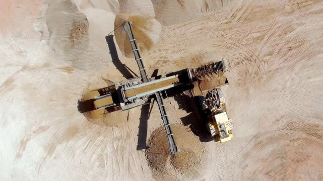 Aerial view of sand quarry with conveyor belt system and yellow front-end loader in Latvia.