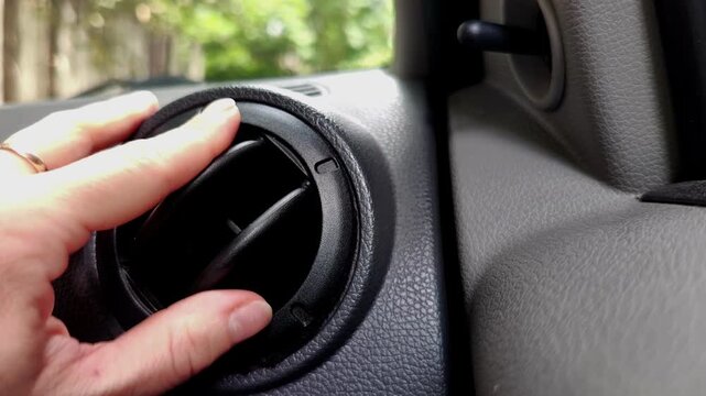 Woman opens a black dashboard air vent inside a gray car interior, climate control, vehicle controls, automotive design, modern transportation.