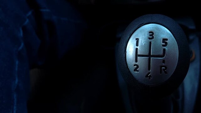 Illuminated manual gear shift lever inside a dark car interior with a blurred driver leg, driving controls, automotive design, transportation concept.