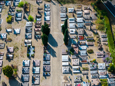 Aerial view of the cemetery with rows of gravestones, stone pathways, and tall cypress trees casting long shadows on the ground in Neuf-Brisach, Grand Est, France.