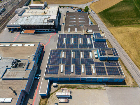 Aerial view of the Daniken storage area featuring large industrial buildings with extensive solar panel arrays on the rooftops, surrounded by roads and fields in Daniken, Solothurn, Switzerland.
