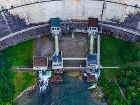 Aerial view of the Barrage de Rossens dam featuring concrete walls, water outlet pipes, and surrounding greenery in Pont-la-Ville, Fribourg, Switzerland.