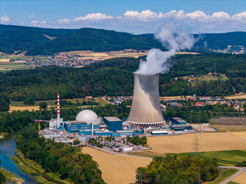 Aerial view of Gosgen-Daniken Nuclear Power Plant with its cooling tower emitting steam, situated along the Aare river amidst forests and fields in Daniken, Solothurn, Switzerland.