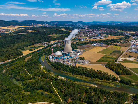 Aerial view of Gosgen-Daniken Nuclear Power Plant with cooling tower emitting steam, situated along the Aare River amidst fields and forests in Daniken, Solothurn, Switzerland.
