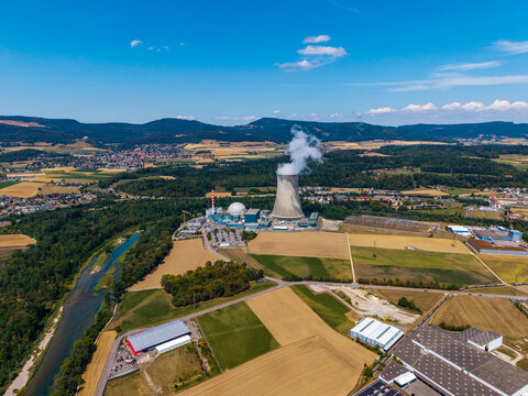 Aerial view of the Gosgen-Daniken Nuclear Power Plant with its cooling tower emitting steam, situated amidst agricultural fields and the Aare river in Daniken, Solothurn, Switzerland.