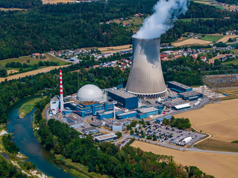 Aerial view of Gosgen-Daniken Nuclear Power Plant featuring its large cooling tower and reactor building set beside a river and lush green landscape in Daniken, Solothurn, Switzerland.