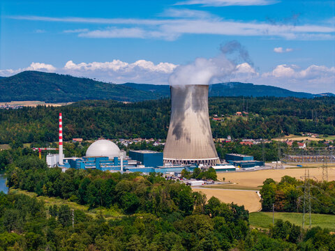 Aerial view of Gosgen-Daniken Nuclear Power Plant with its prominent cooling tower emitting steam, surrounded by lush forests and agricultural fields in Daniken, Solothurn, Switzerland.