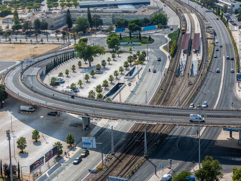 Aerial view of the Alges roundabout and railway station infrastructure surrounded by urban roads and palm trees in Alges, Lisbon, Portugal.