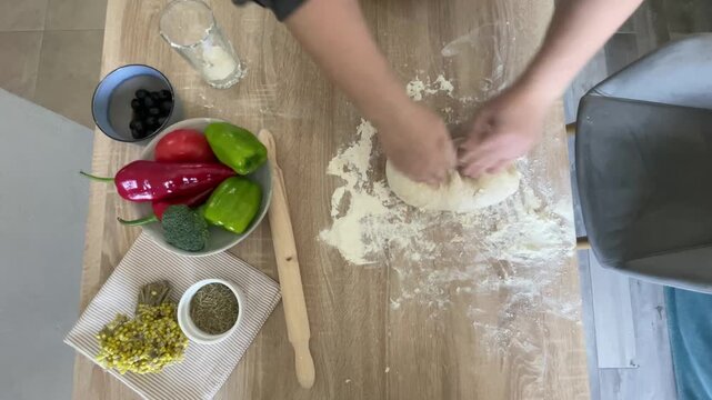 The hands of a female cook knead a lump of dough on a wooden table with white wheat flour.