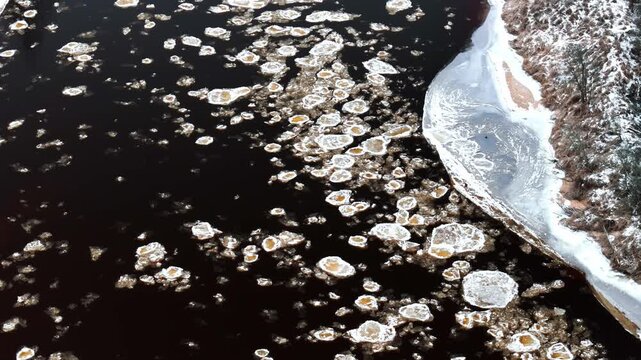 Aerial view of ice floes drifting on the dark water of the Daugava River near the snow-covered banks in Riga, Latvia.