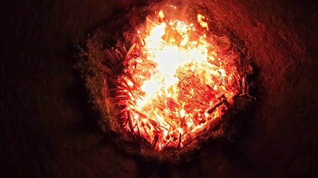 Aerial view of a bright bonfire burning at night with glowing embers and crackling wood in the darkness of Riga, Latvia.