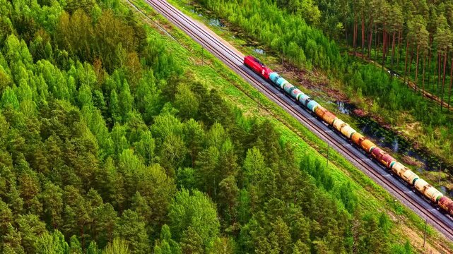 Aerial view of a long freight train transporting cargo through a dense green forest landscape in Riga, Latvia.