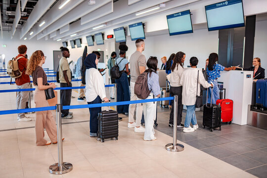 Passengers waiting in line at airport check-in counter with luggage